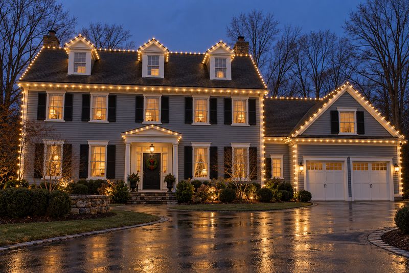 Gray colonial with roofline, dormers and portico outlined in warm white lights