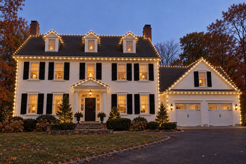 White colonial at dusk among fall foliage with roofline outlined